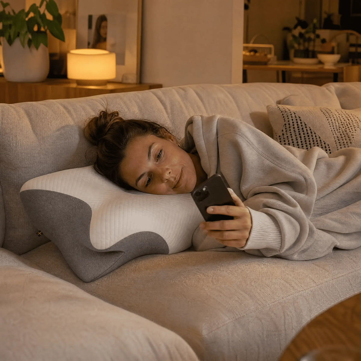 Kvinna som vilar på ergonomisk sovkudde i soffan och använder mobiltelefon hemma