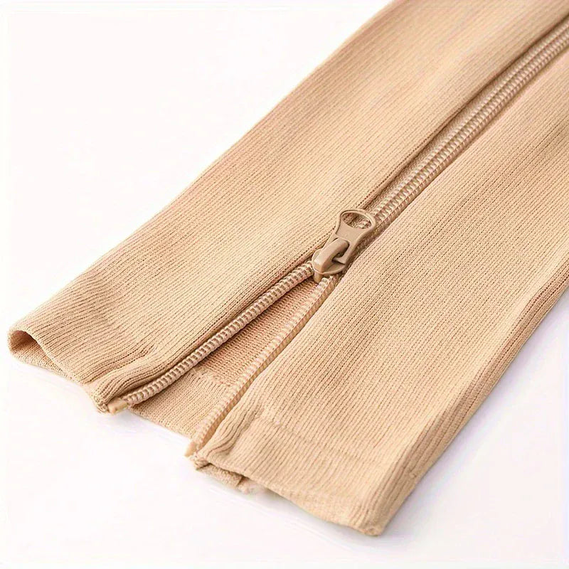 Närbild på beige stödstrumpor med sidoblixtlås och ribbat material.