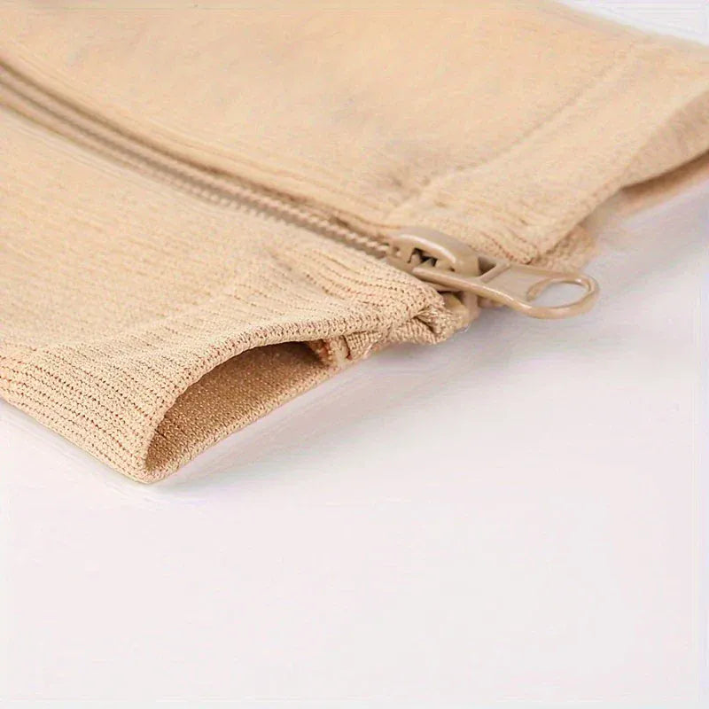 Närbild på sidoblixtlåset och det ribbade materialet på en beige stödstrumpa.